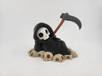 Grim Reaper Relaxing on Skulls – Tristo Mietitore sui Teschi