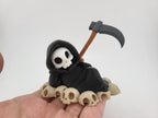 Grim Reaper Relaxing on Skulls – Tristo Mietitore sui Teschi