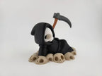 Grim Reaper Relaxing on Skulls – Tristo Mietitore sui Teschi