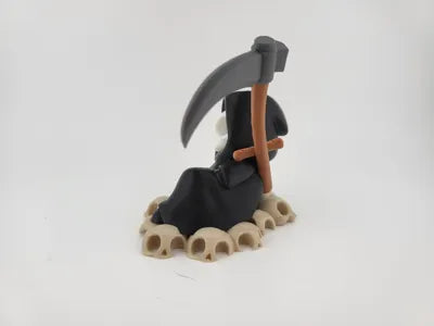 Grim Reaper Relaxing on Skulls – Tristo Mietitore sui Teschi
